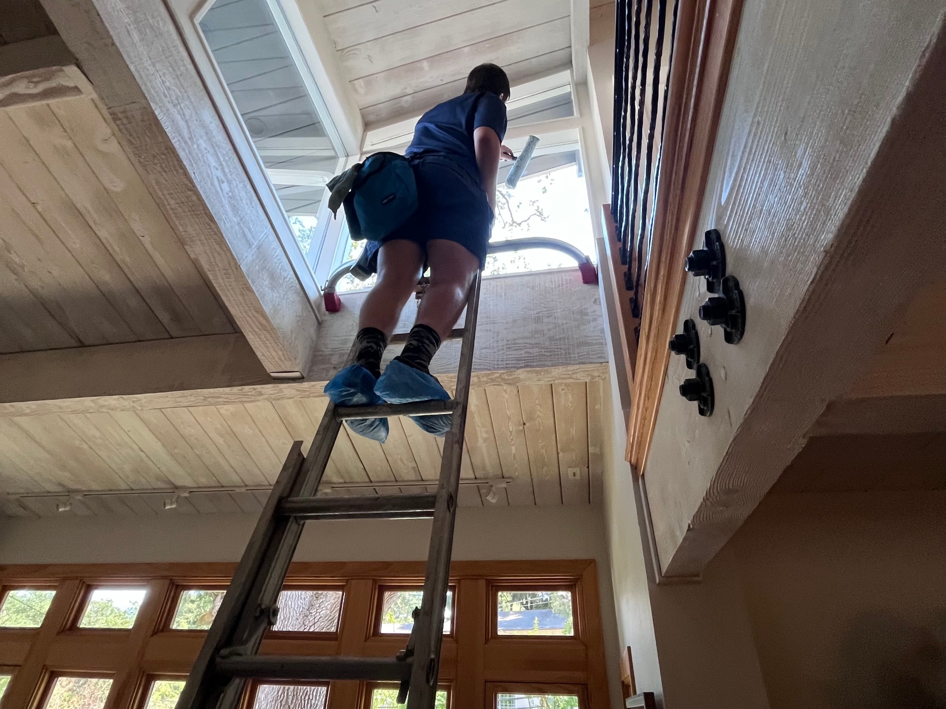 Professional interior window cleaning on a ladder in a high-ceiling home